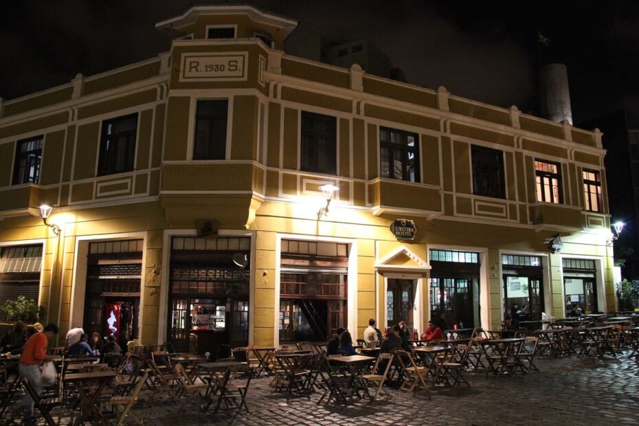 Casarão histórico iluminado com mesas de bares na calçada do Largo da Ordem à noite, no centro de Curitiba