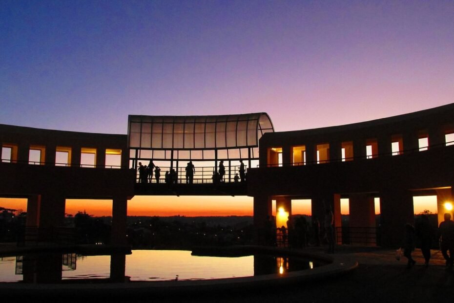 Mirante do Parque Tanguá em silhueta ao pôr do sol, com céu alaranjado refletido no espelho d'água, em Curitiba