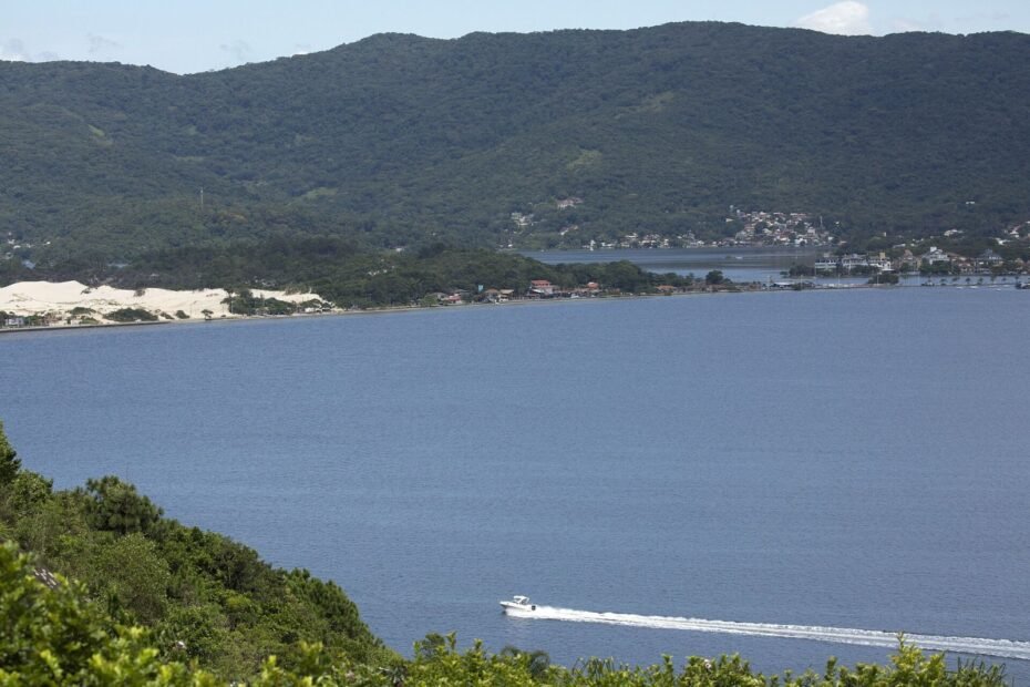 Lancha cruzando a Lagoa da Conceição, com as dunas e os morros verdes ao fundo, em Florianópolis (SC)