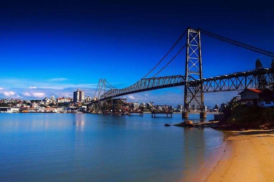 Ponte Hercílio Luz refletida nas águas calmas da baía, sob céu azul intenso, em Florianópolis (SC)