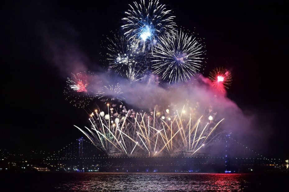 Queima de fogos de Réveillon sobre a Ponte Hercílio Luz iluminada, refletida no mar, em Florianópolis (SC)