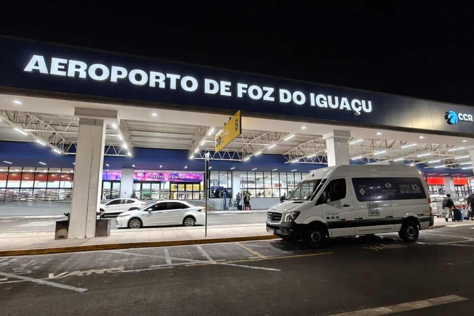 Terminal do Aeroporto Internacional de Foz do Iguaçu (PR) iluminado à noite, com van estacionada na entrada