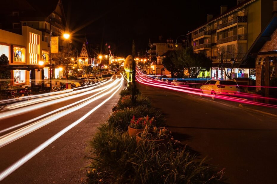 Rastros de luz dos carros em avenida do centro de Gramado à noite, entre lojas e prédios alpinos