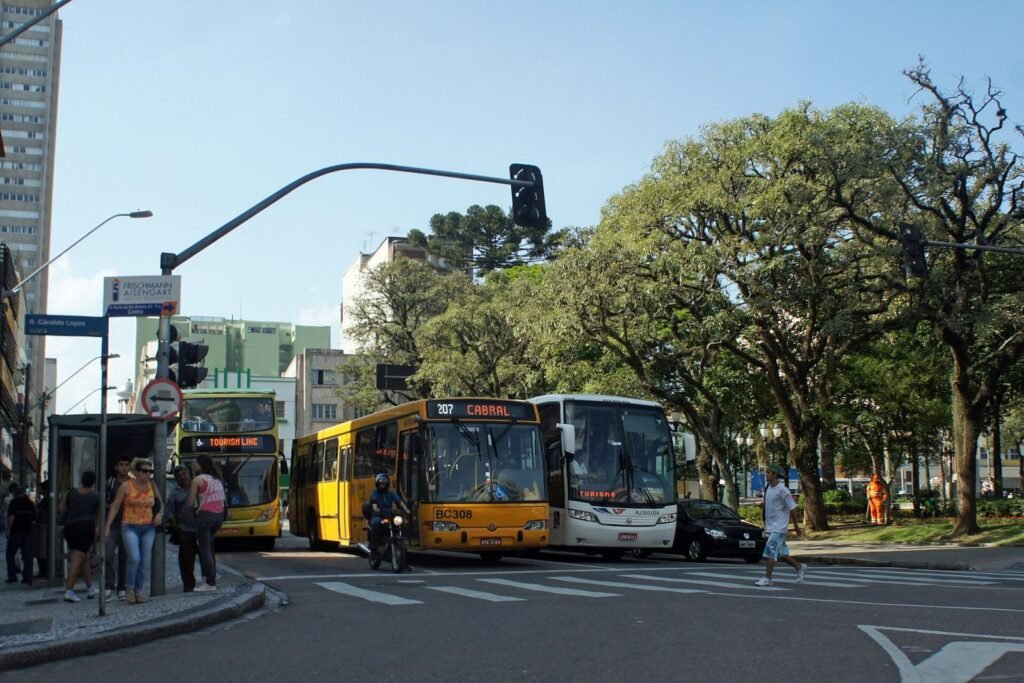 Ônibus de dois andares da Linha Turismo e ônibus urbanos em rua arborizada do Centro de Curitiba