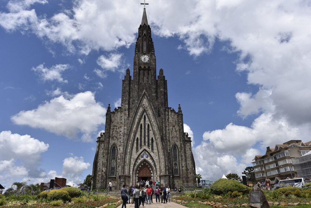 Fachada da Catedral de Pedra sob céu azul com nuvens, no centro de Canela (RS)