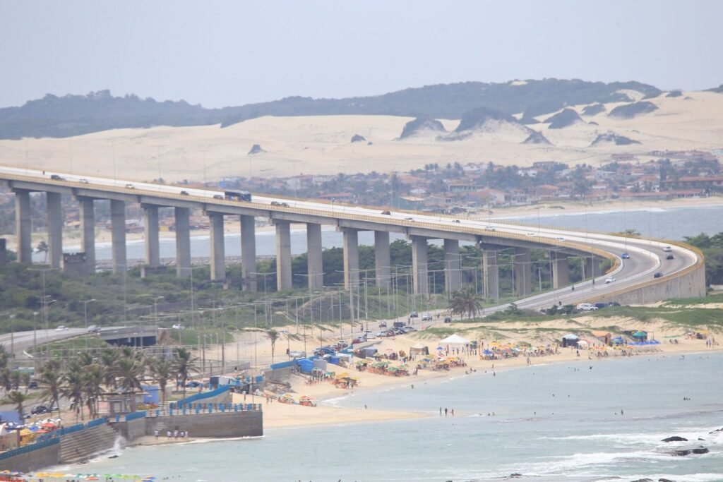 Ponte Newton Navarro sobre o Rio Potengi, com dunas ao fundo e praia urbana em primeiro plano, em Natal (RN)