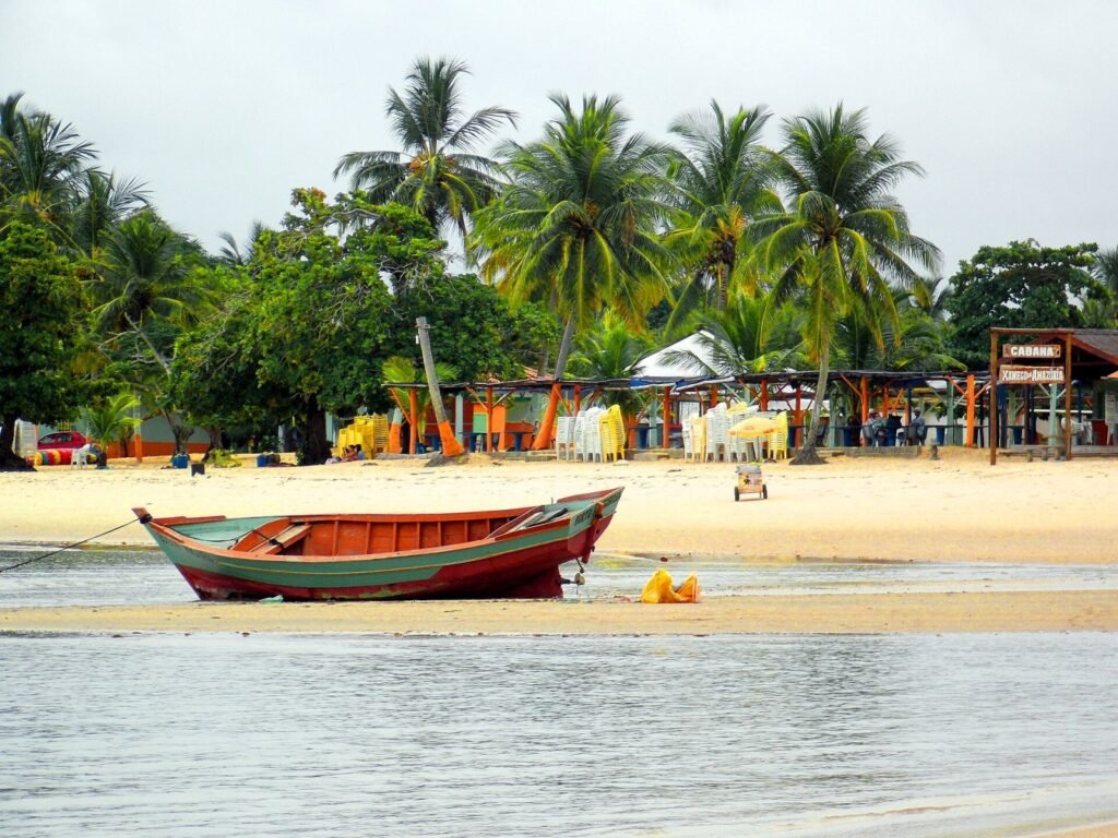 Barco de pesca num banco de areia na Praia de Coroa Vermelha, com coqueiros e barracas, em Santa Cruz Cabrália