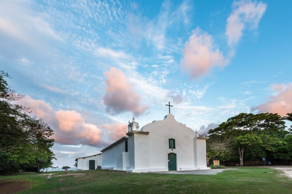 Igreja de São João Batista no Quadrado de Trancoso sob céu azul com nuvens rosadas, em Porto Seguro