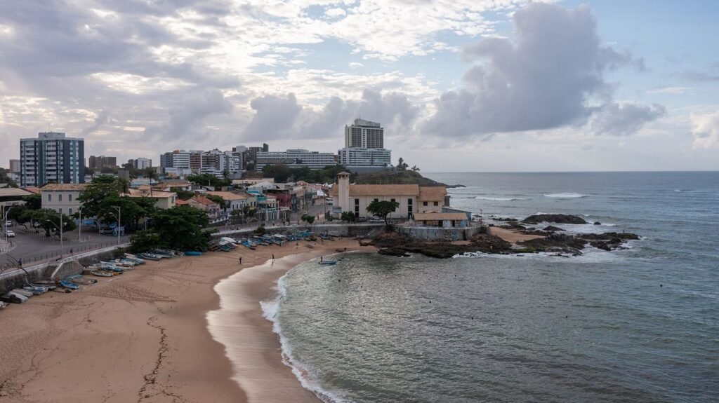Vista aérea da orla do Rio Vermelho, com barcos de pescadores na areia e prédios ao fundo, em Salvador