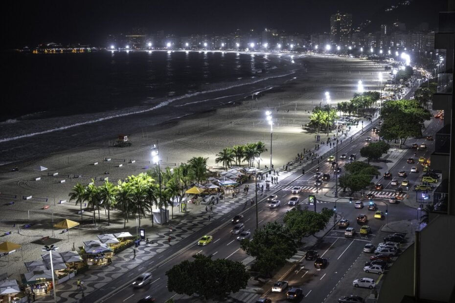 Praia de Copacabana e Avenida Atlântica iluminadas à noite, com quiosques no calçadão, no Rio de Janeiro