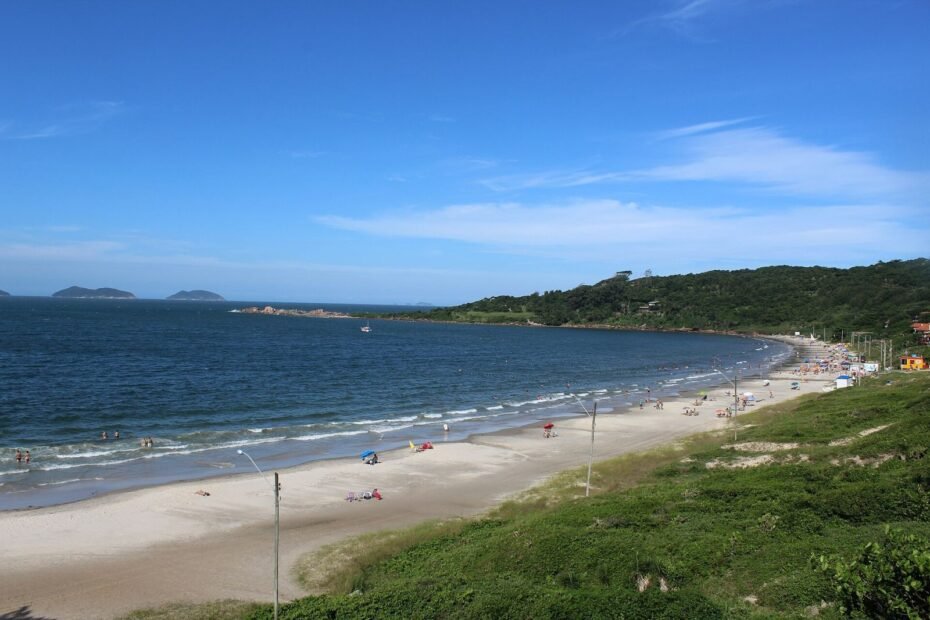 Faixa de areia da Praia de Cima, na Pinheira, com mar azul e morro verde, em Palhoça (SC)